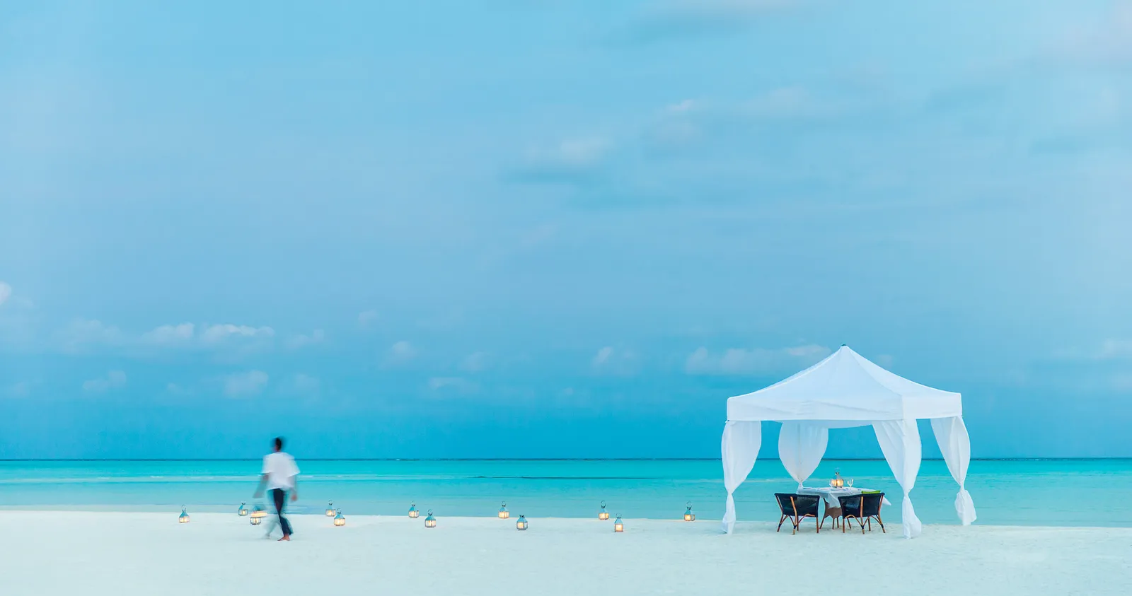 A white gazebo with a table laid on the sandbank, and a waiter on his way