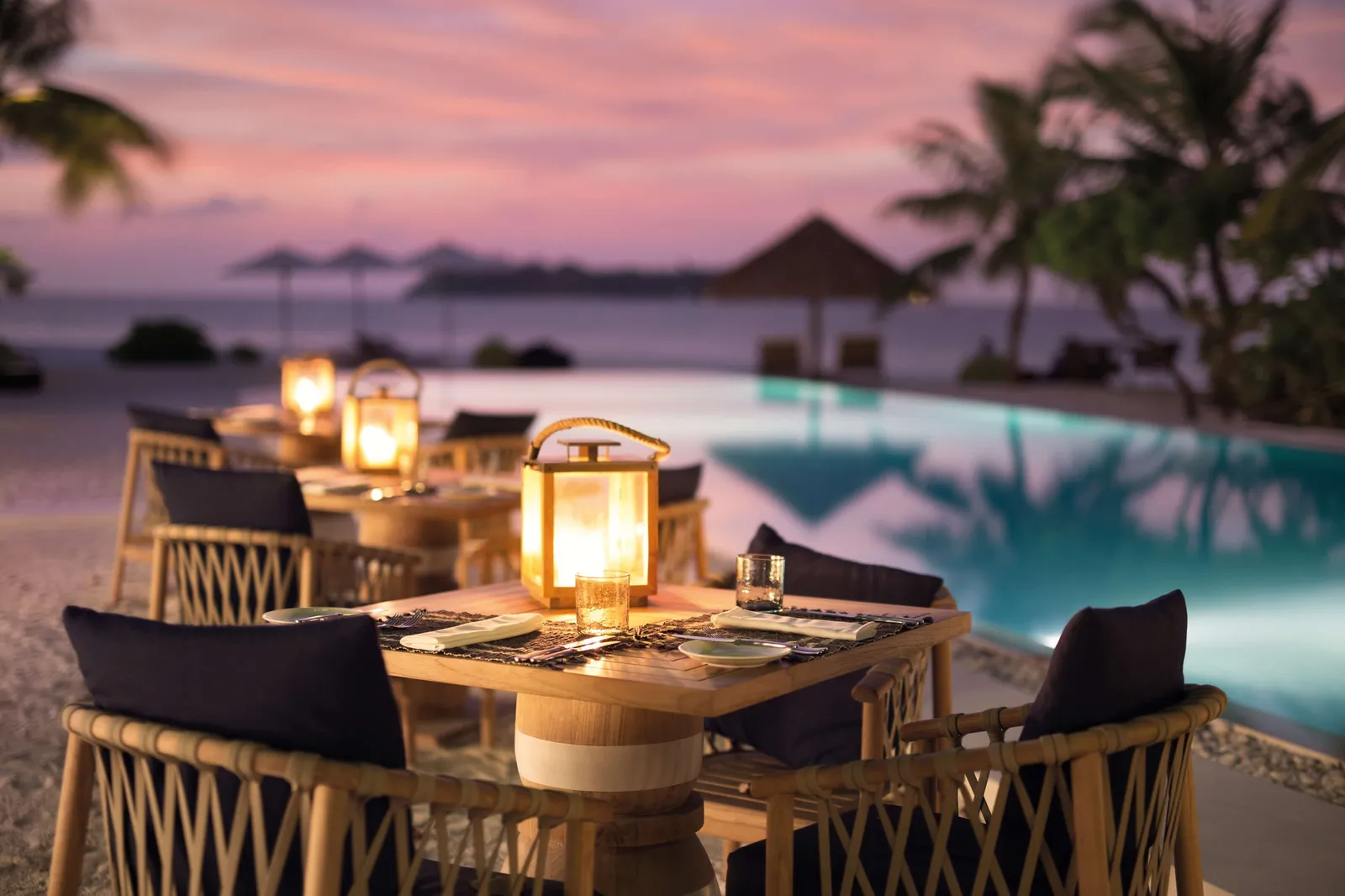 Restaurant tables at dusk, lanterns lit beside the pool