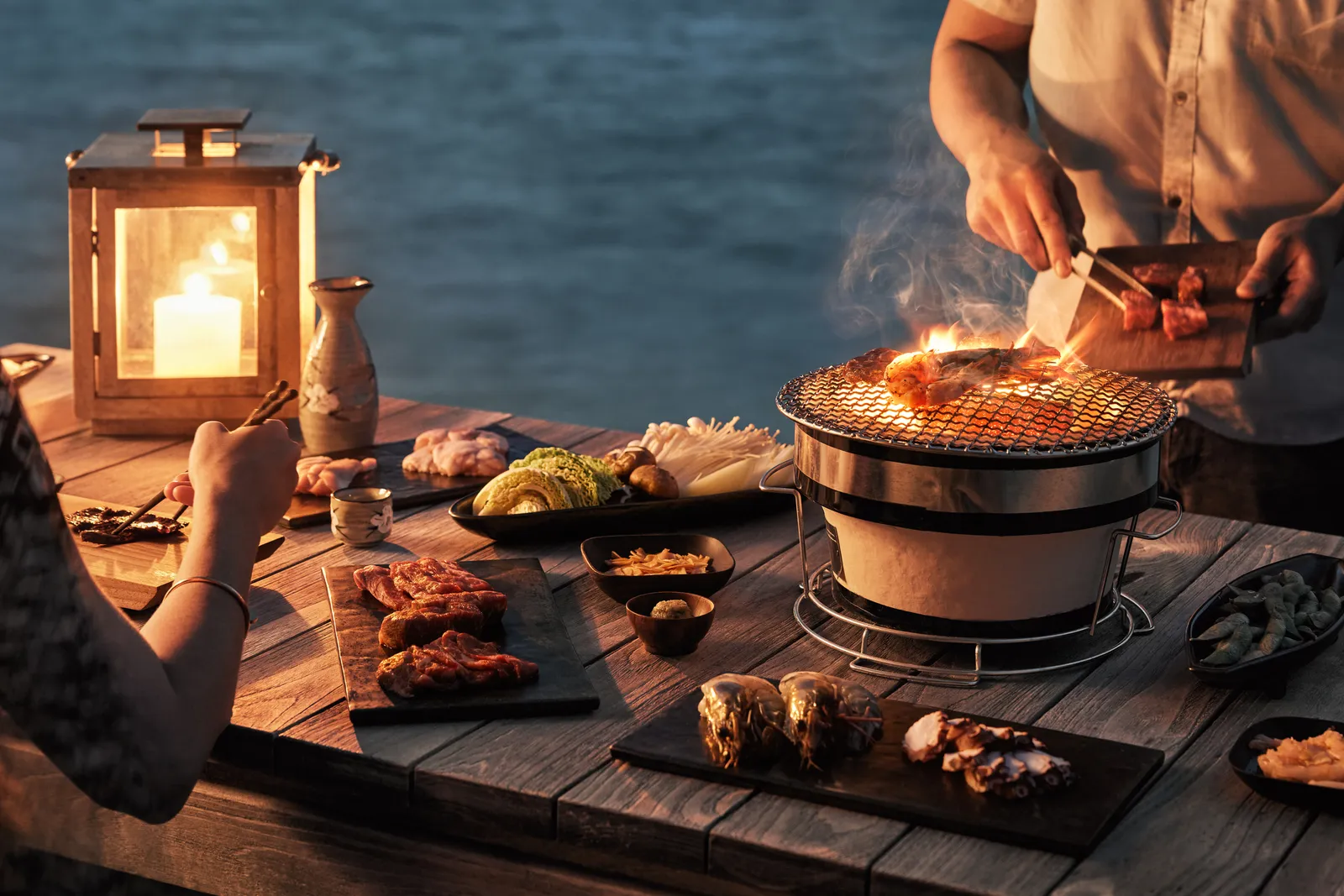 Meat and vegetables grilled on a brazier, a lantern lit on the wooden table