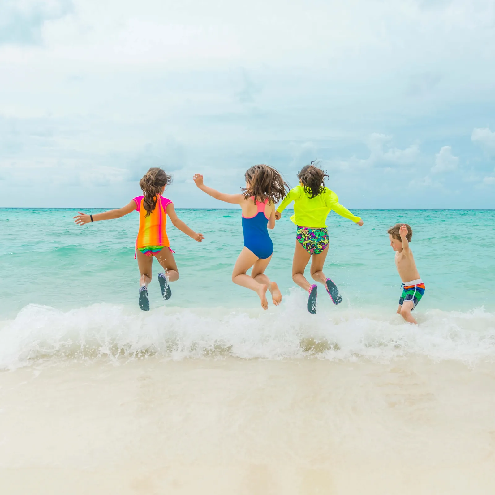 4 children jumping through the shallow waves of the lagoon, on the white-sand shore.