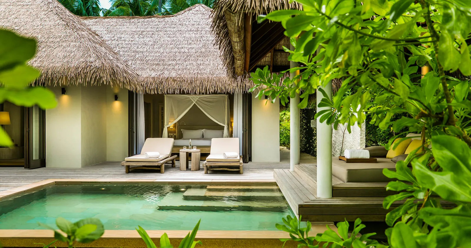 A Beach Villa under its thatched roof, with loungers and its private pool among the greenery.