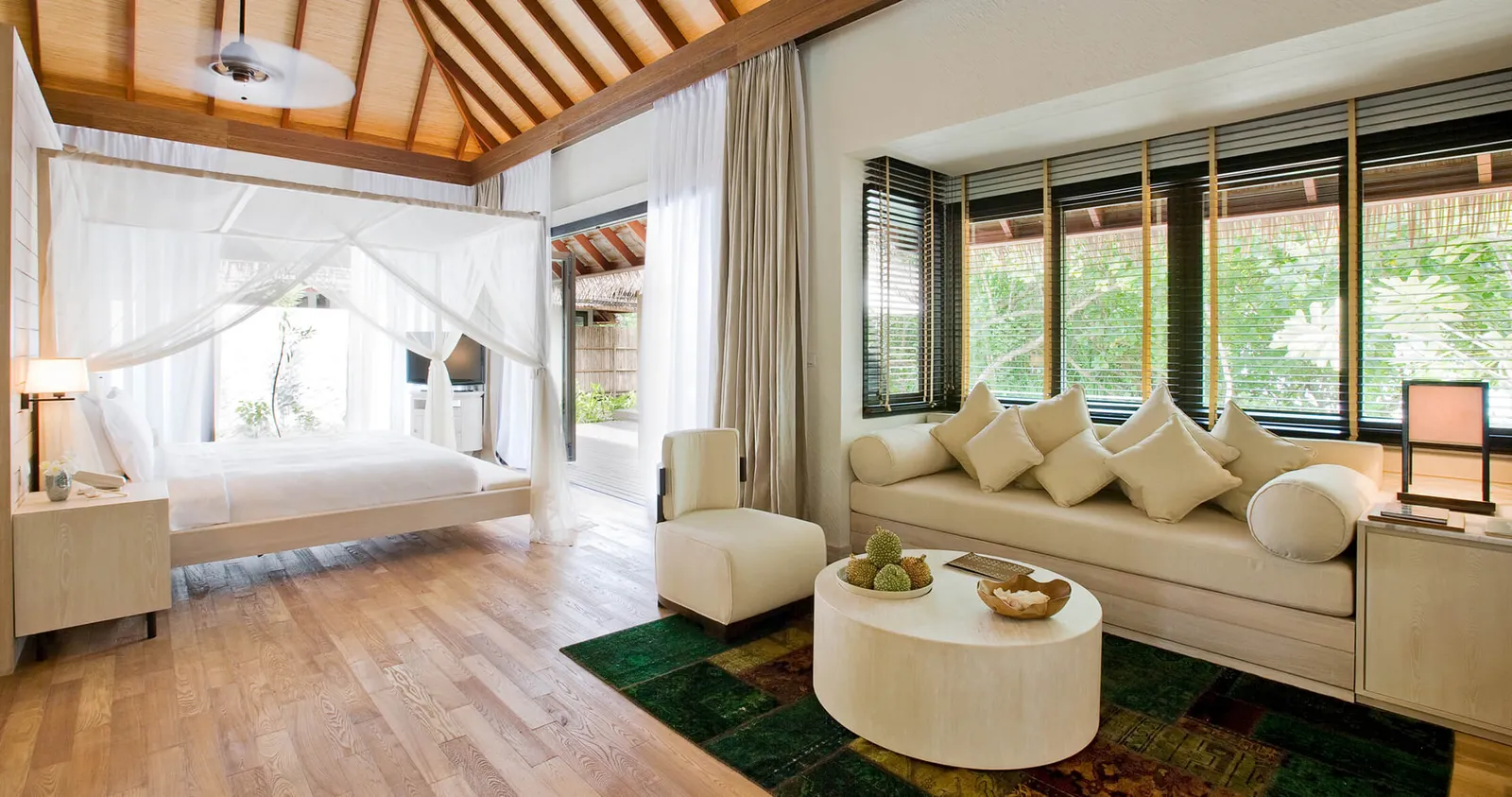 The sitting room of a 2-bedroom Beach Suite, with the sofa, the canopy bed of the bedroom and windows on the garden.