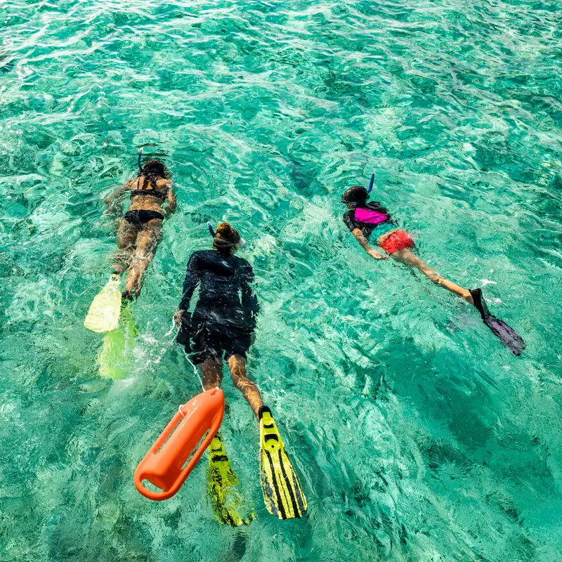 3 people snorkelling over the pale sand of the lagoon.