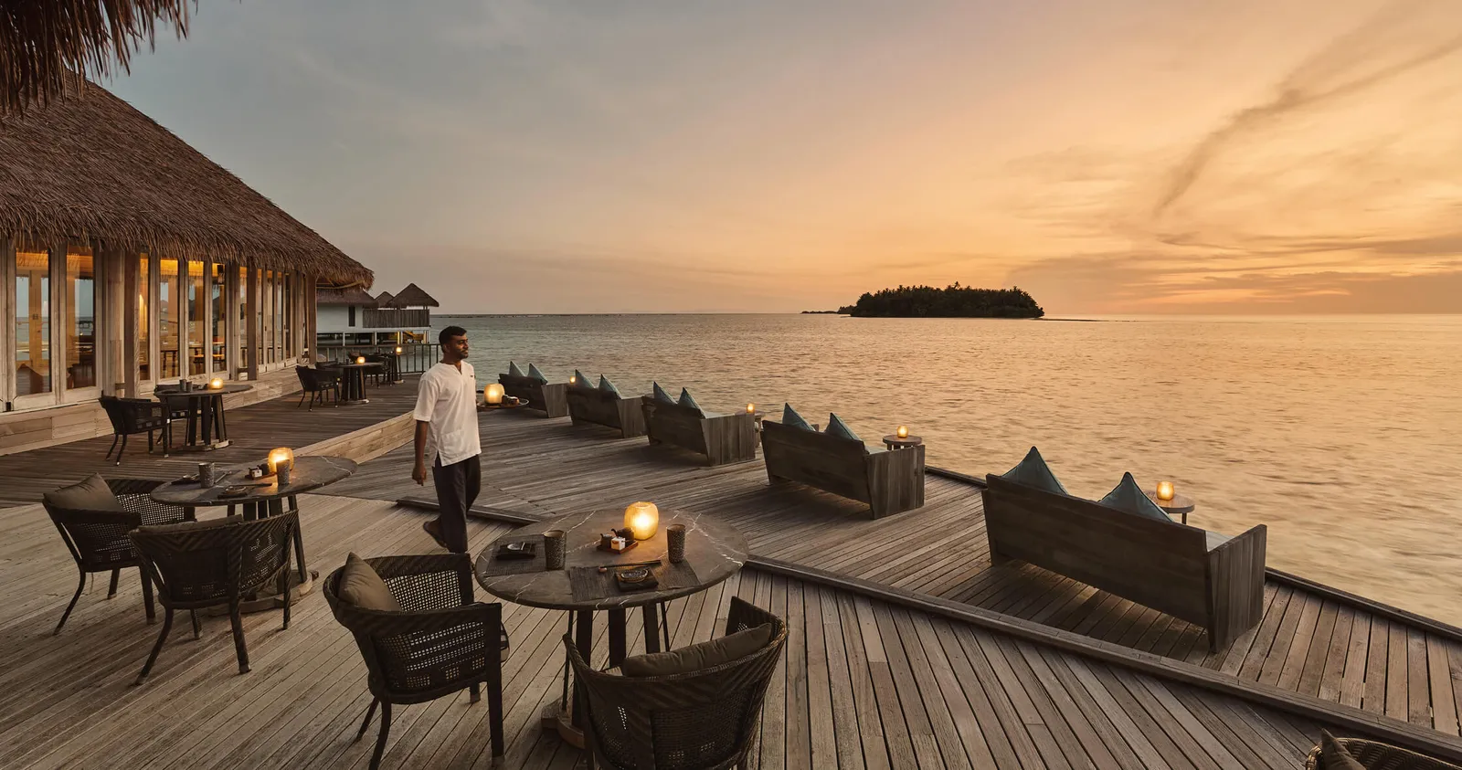 Tai’s deck at sunset, with timber armchairs, lanterns on the tables and a waiter.
