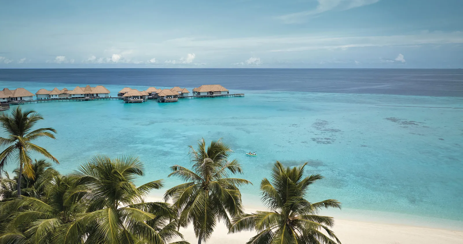 The water villas seen over the palms, in a row on the clear lagoon.