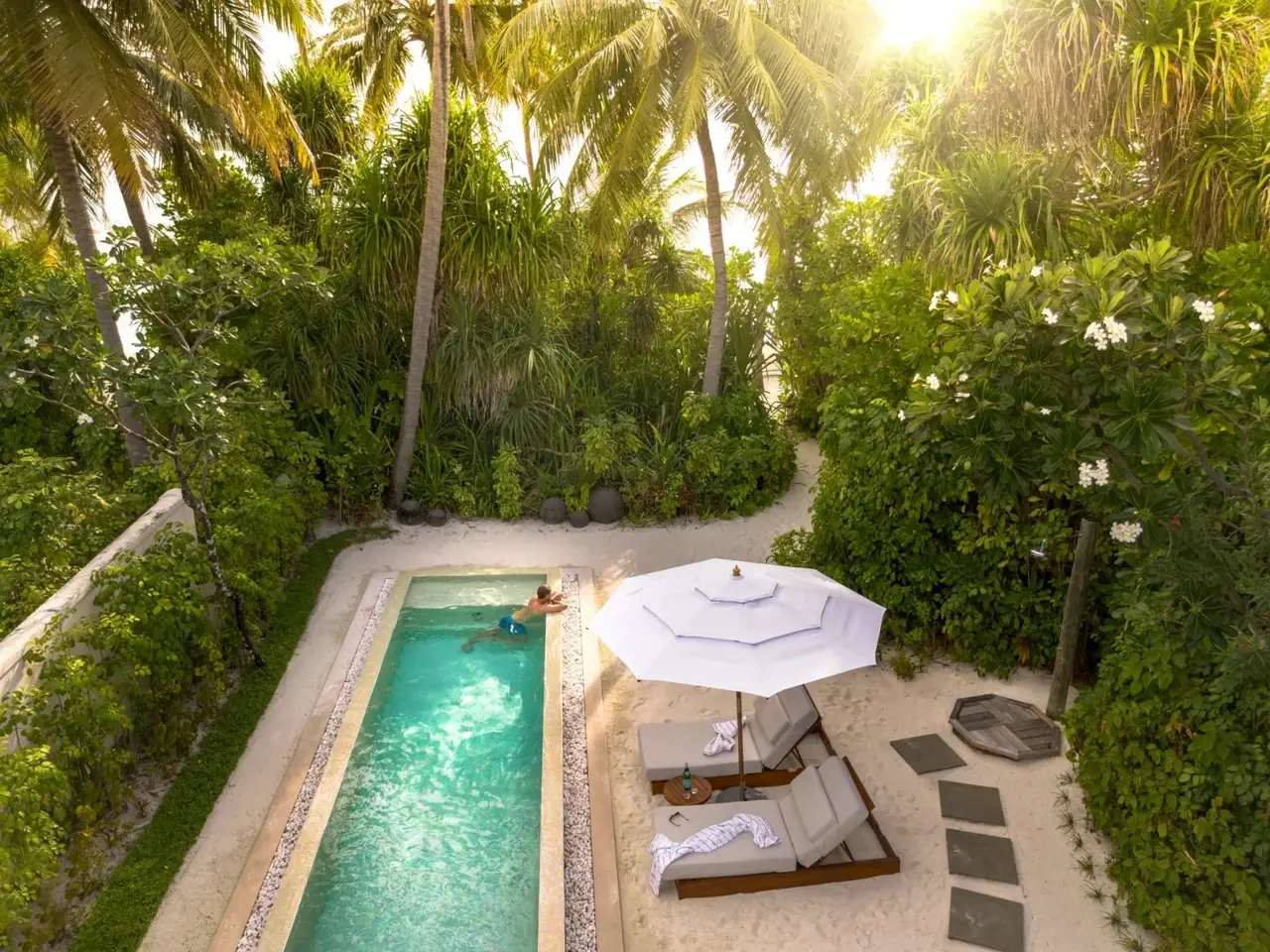 A pool among the greenery, with a parasol and loungers