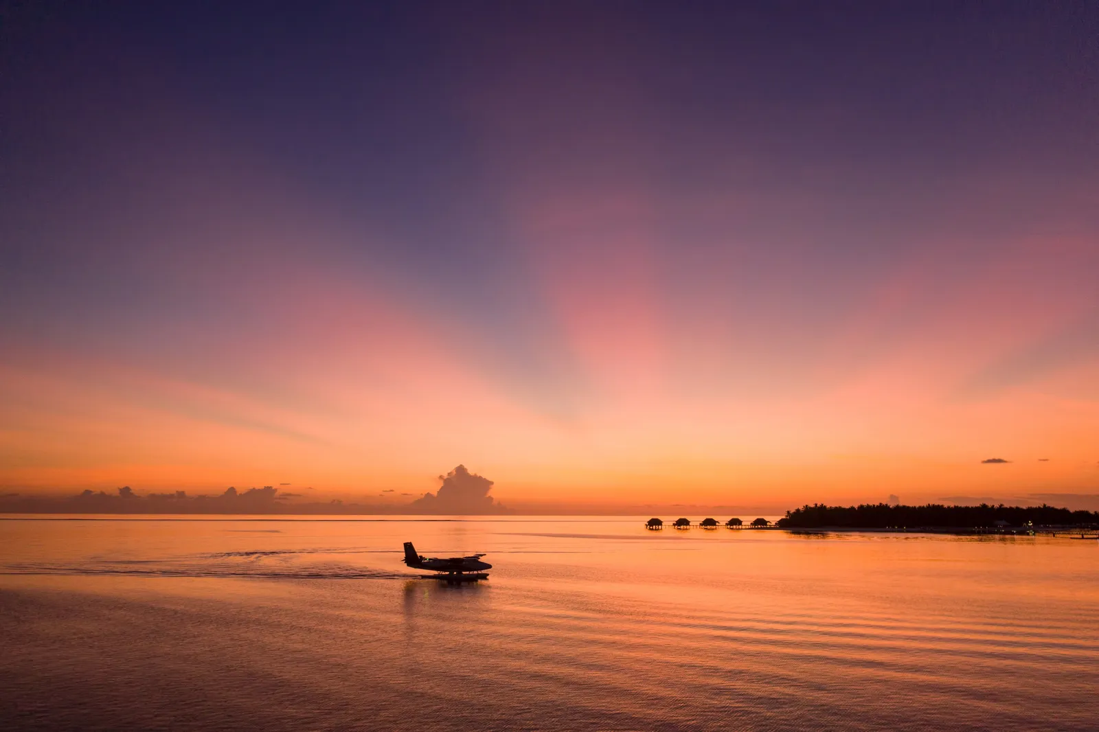 A seaplane on the water at sunset, the water villas on the horizon