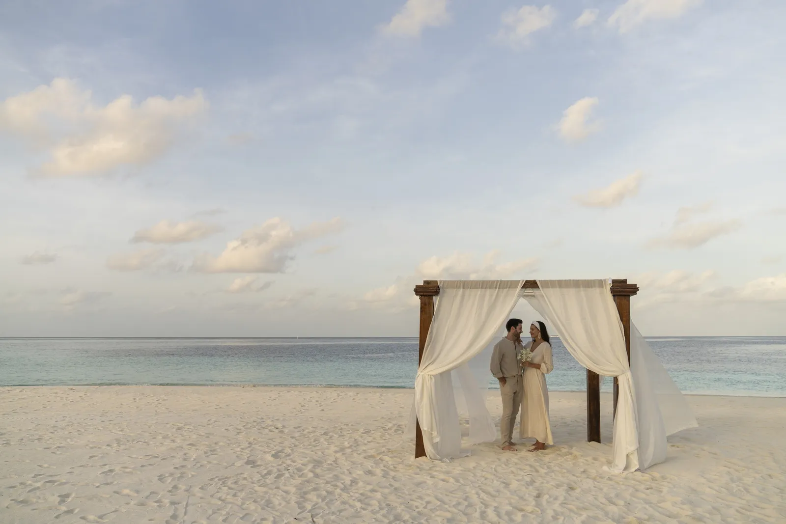 A newly married couple under the white canopy on the beach