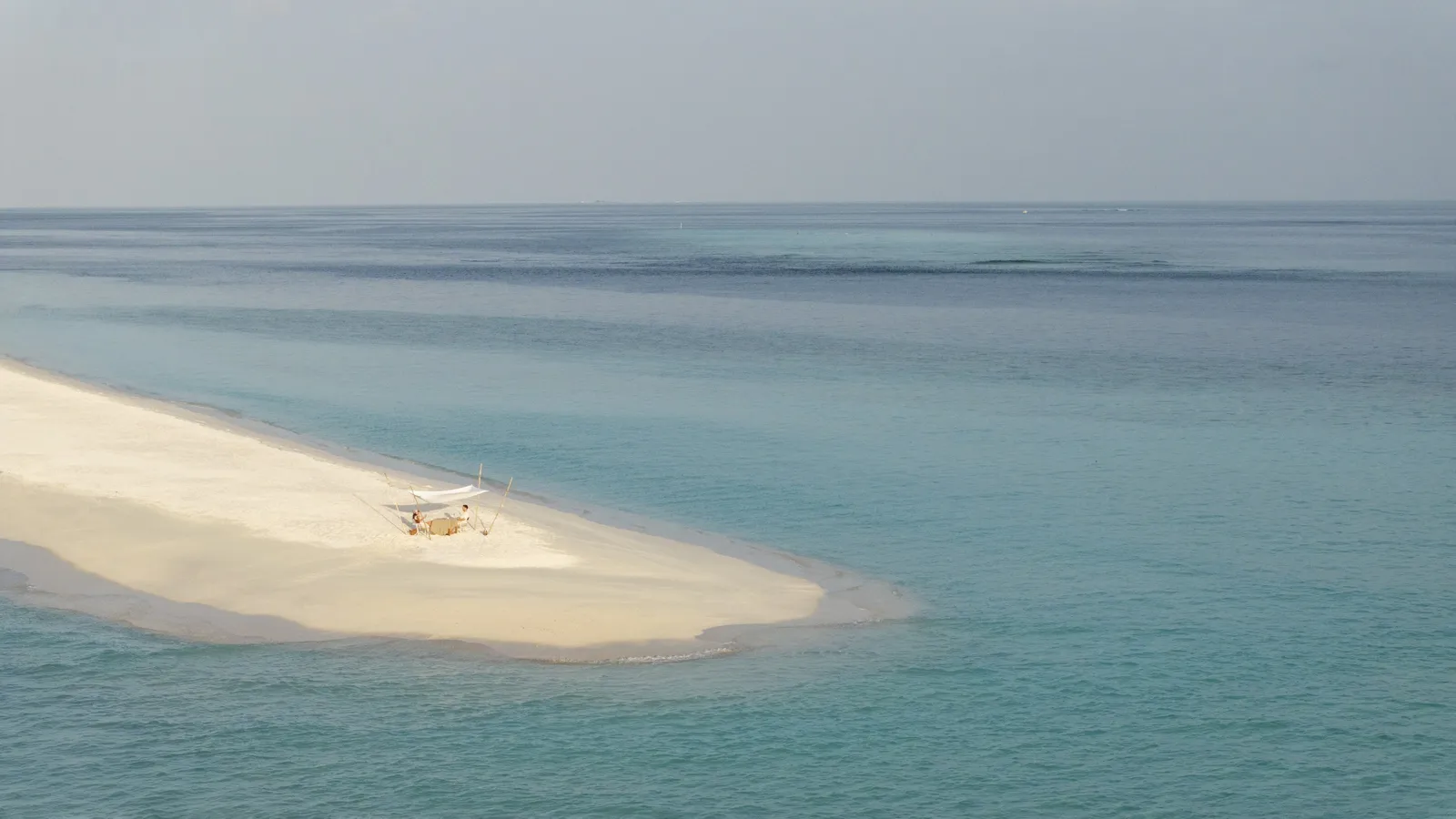 A sandbank in the open sea and a table under a white awning