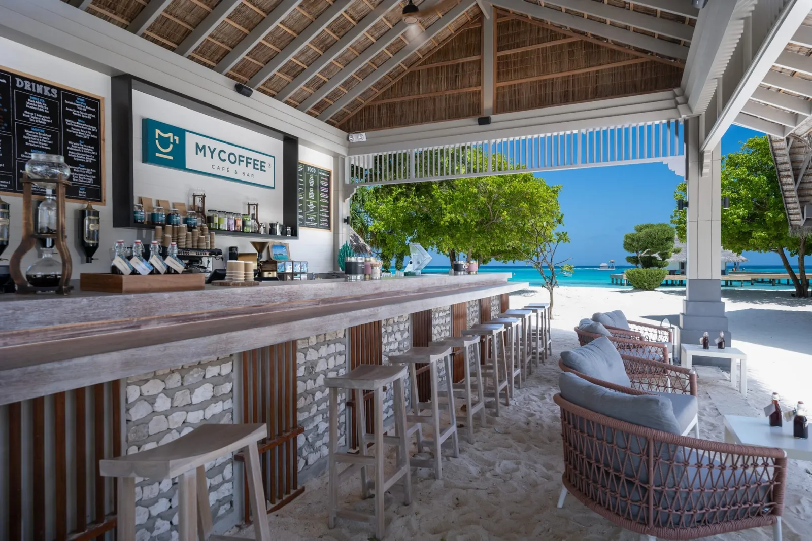 The MYCOFFEE counter under its thatched roof, with the coffee machines, stools and the sea behind.