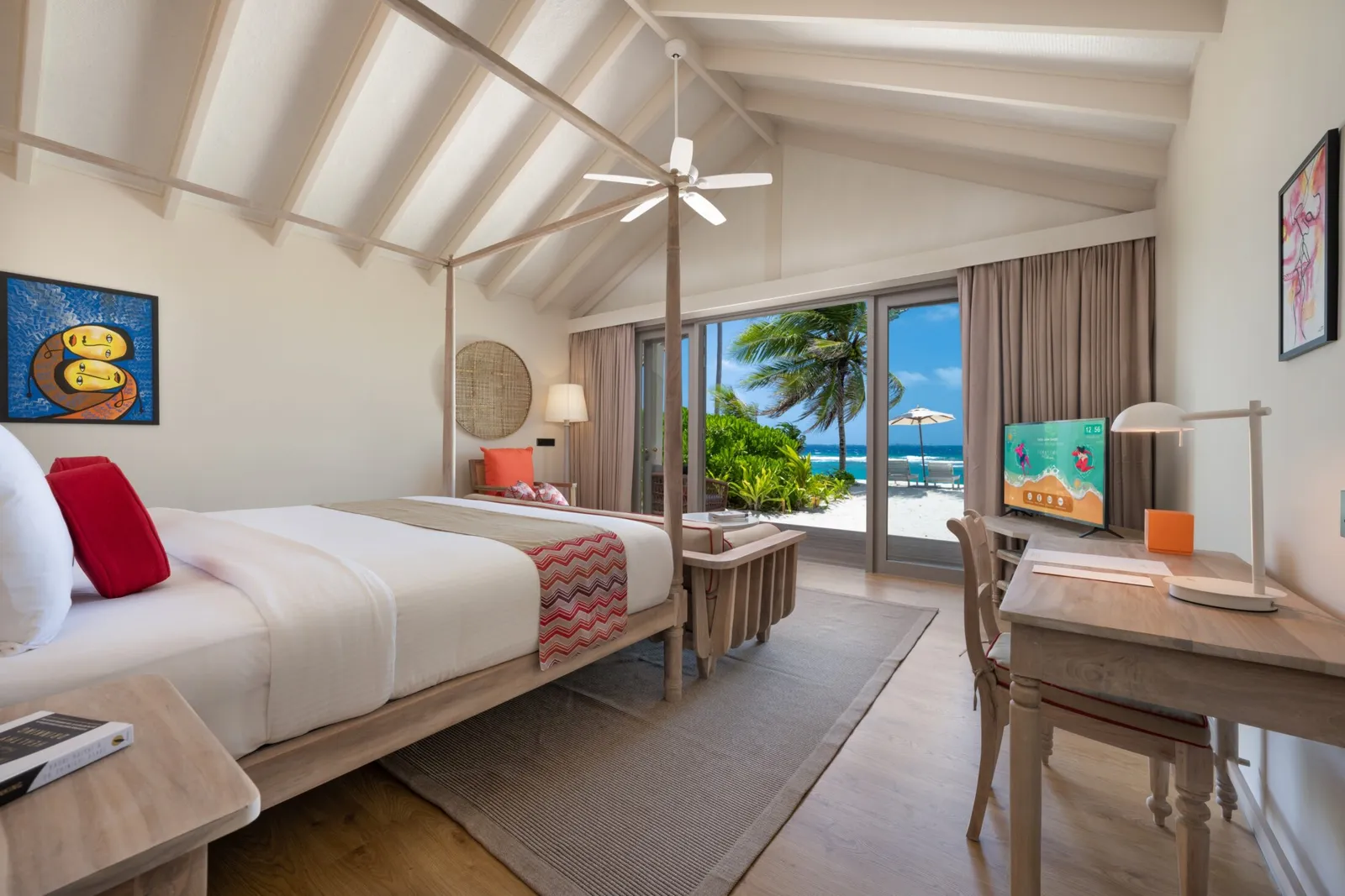 A Beach Villa bedroom: the four-poster king bed, the desk and the glass doors open onto the beach and the sea.