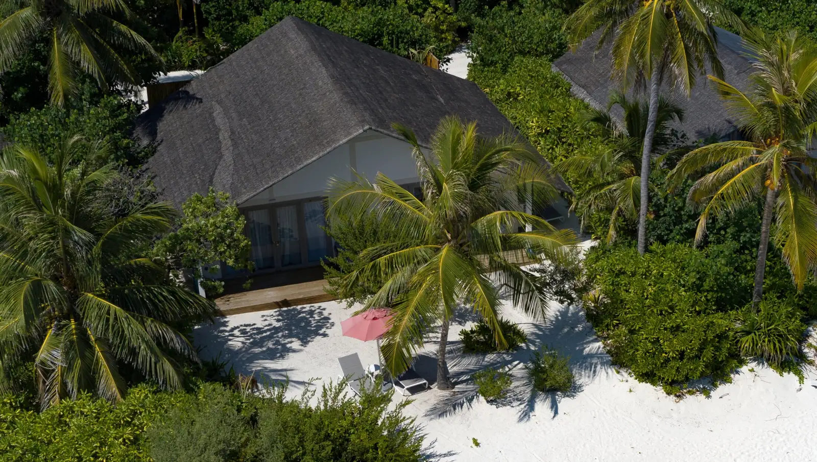 From above, the Two Bedroom Family Beach Villa among the palms, with its deck and a red parasol on the sand.