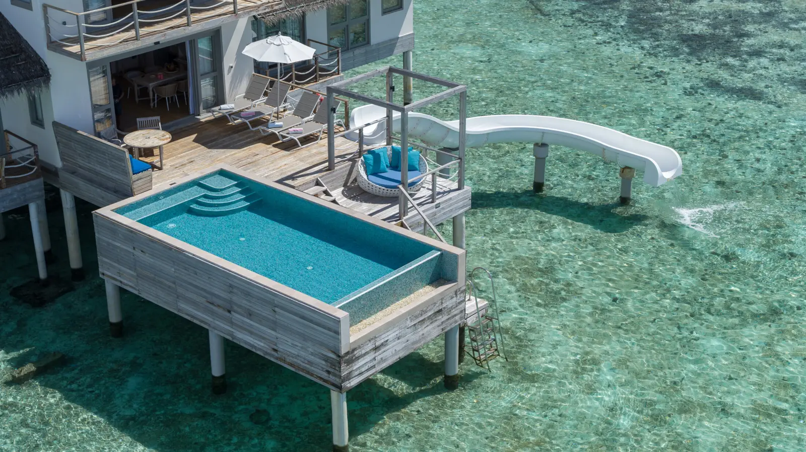 The Two Bedroom Lagoon Pool Villa with Slide from above: the pool on its deck and the white slide ending in the sea.