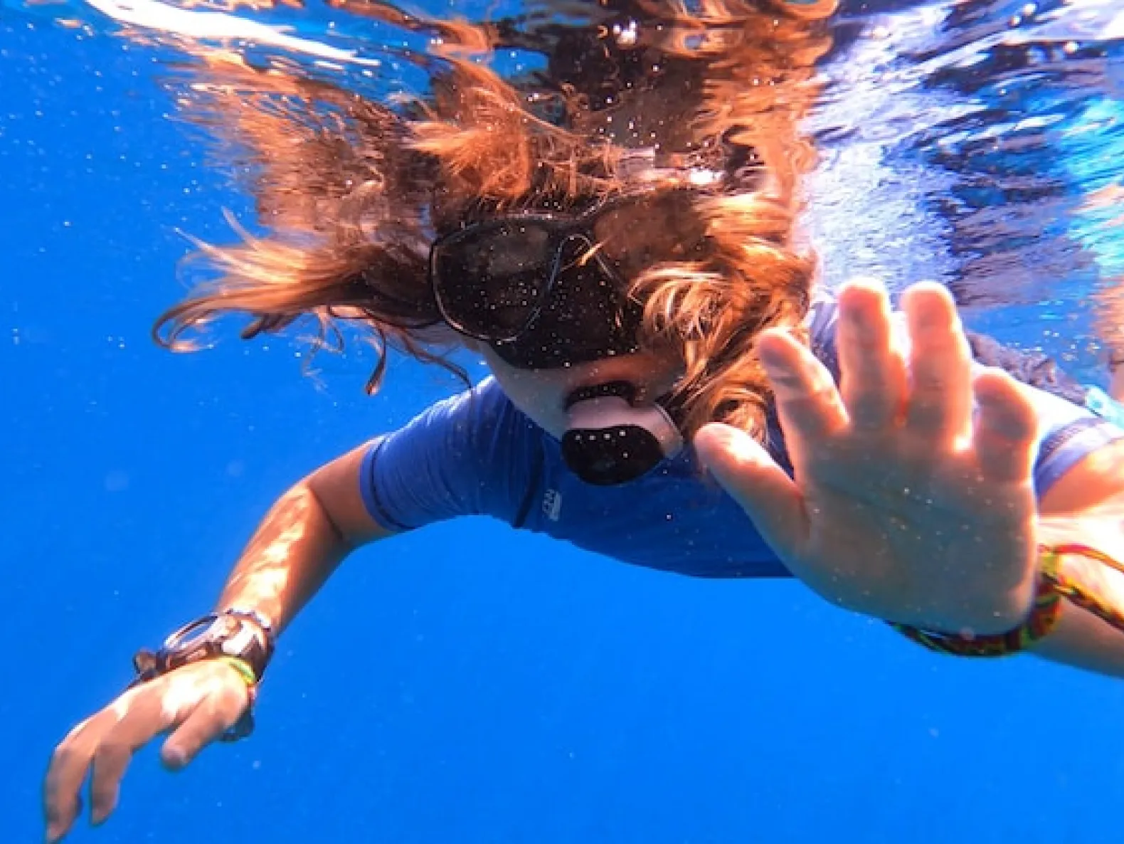 A girl in mask and snorkel swims underwater and waves.