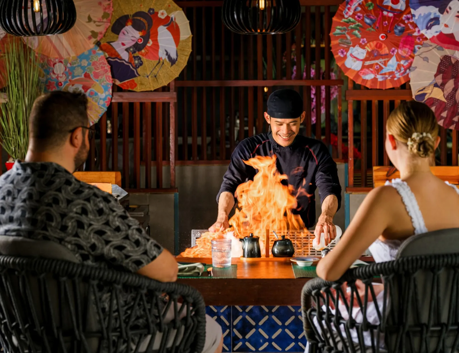 At Teien the teppanyaki chef sends up a flame from the griddle in front of 2 guests, under Japanese parasols.