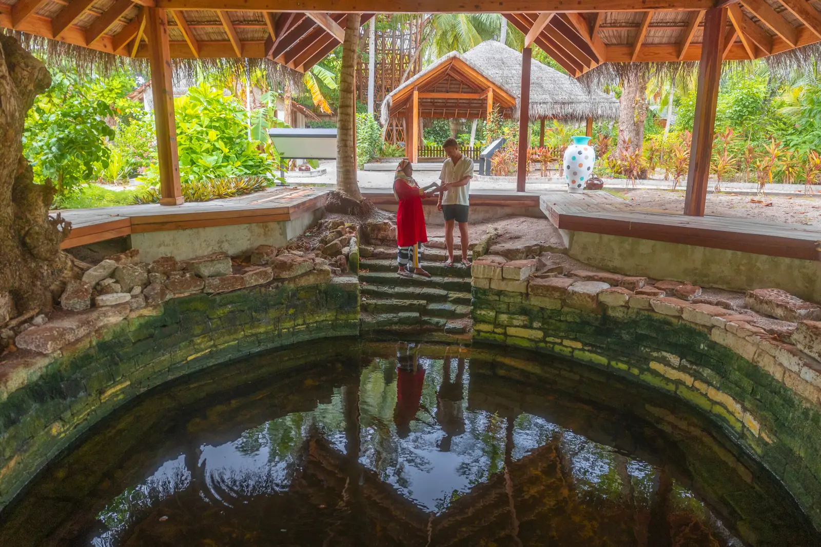 One of the ancient temple tanks in the middle of the island, with its stone steps, and 2 people at its edge among the green.
