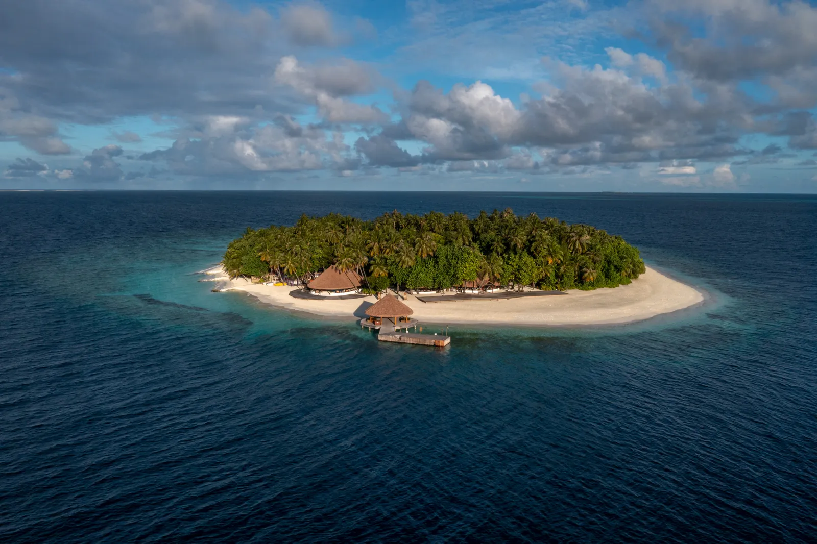 Ihuru from the sea: the small round island covered in palms, its ring of sand and the jetty running into the lagoon.