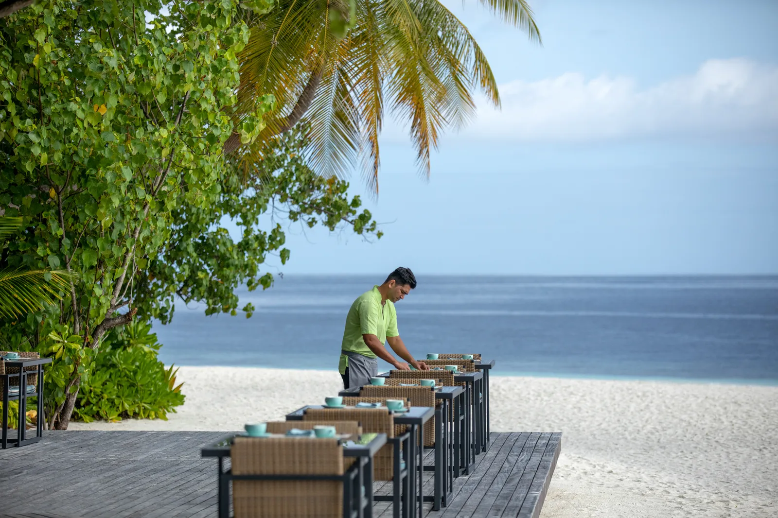 A waiter laying tables on the restaurant’s timber deck at the edge of the beach.