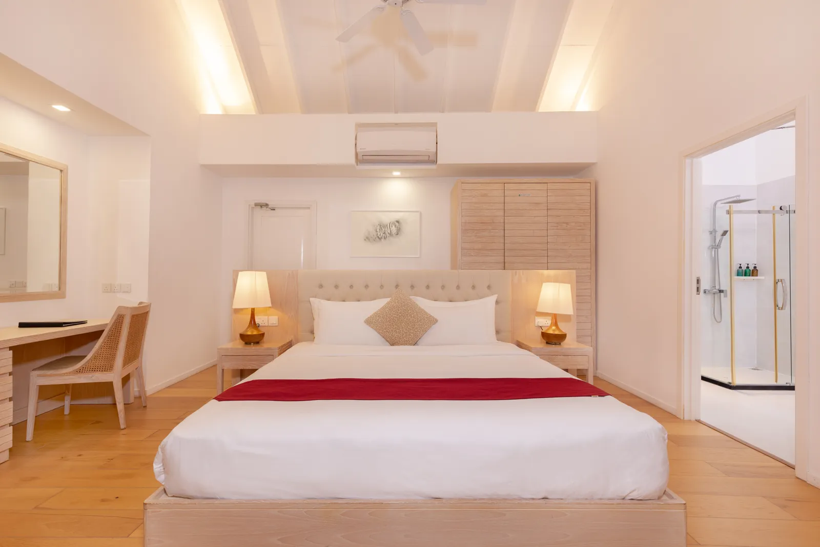 A Water Villa bedroom: king bed, writing desk and a glass-walled shower.