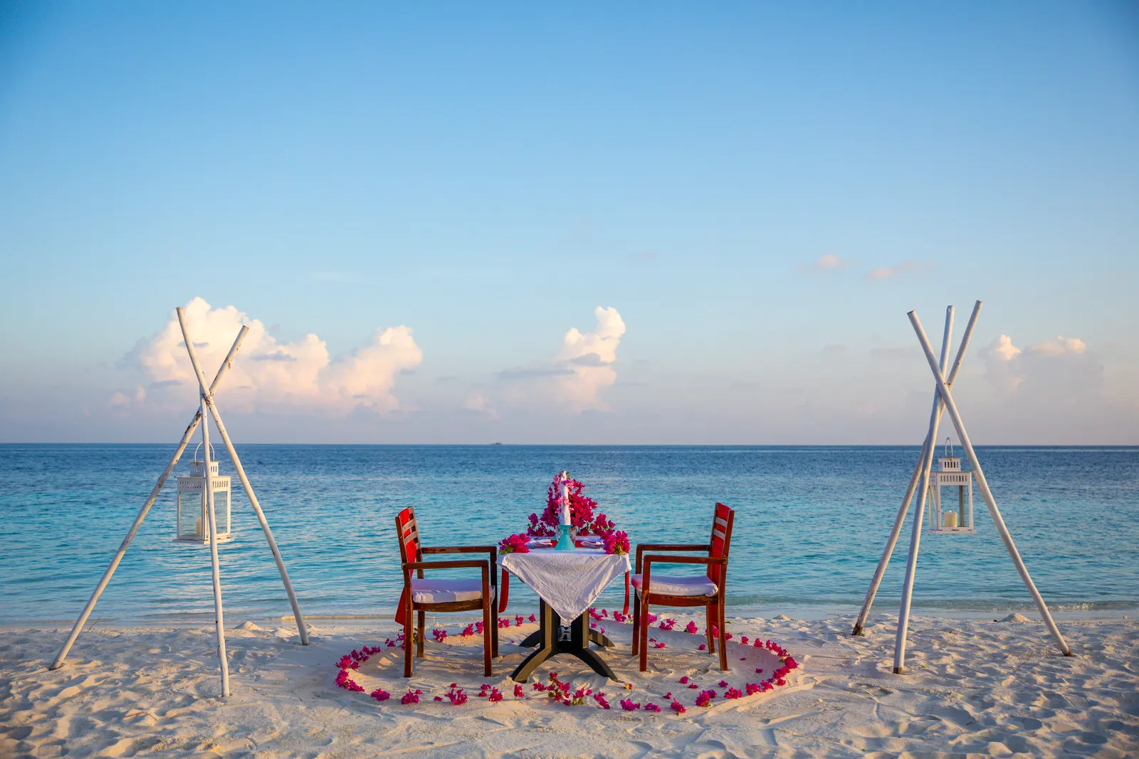 A table for 2 on the beach, a heart of petals on the sand and the sea behind.