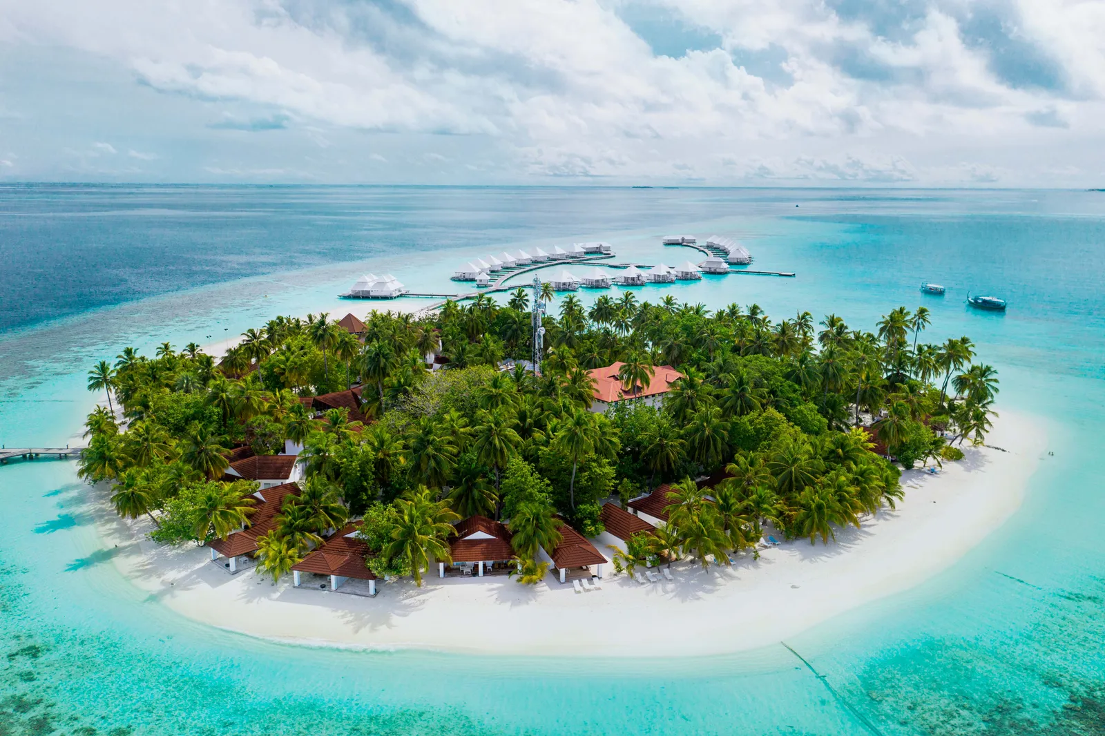 The island from above, its beach villas among the palms and the water villas’ jetty behind.
