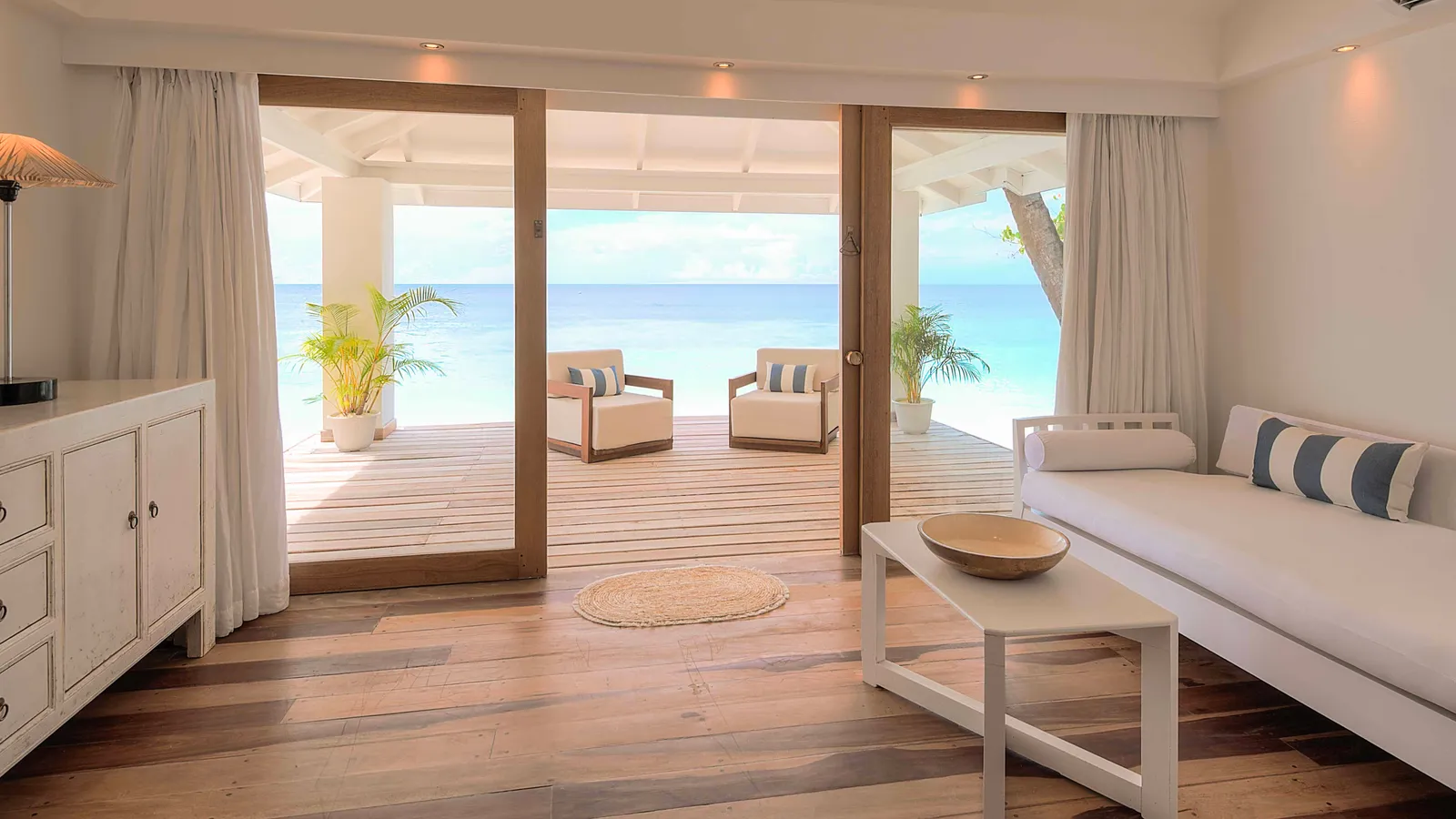 A Beach Front Junior Suite’s living room, with the sofa bed and the glass doors open onto the veranda and the sea.