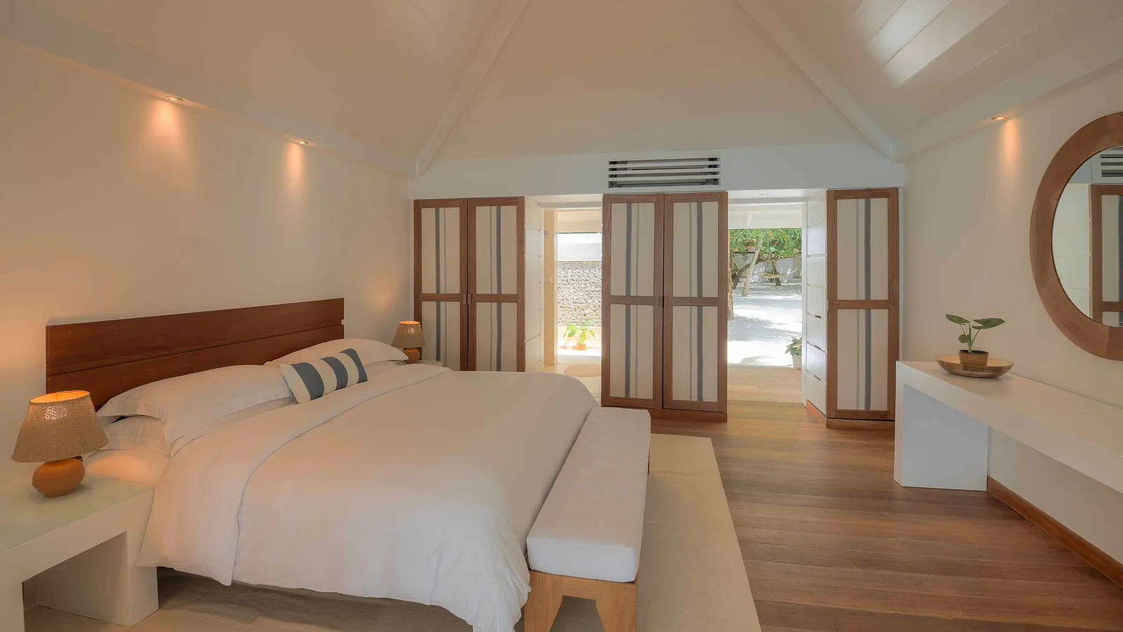 A Beach Front Villa bedroom: the double bed, the wooden floor and the doors open onto the veranda.