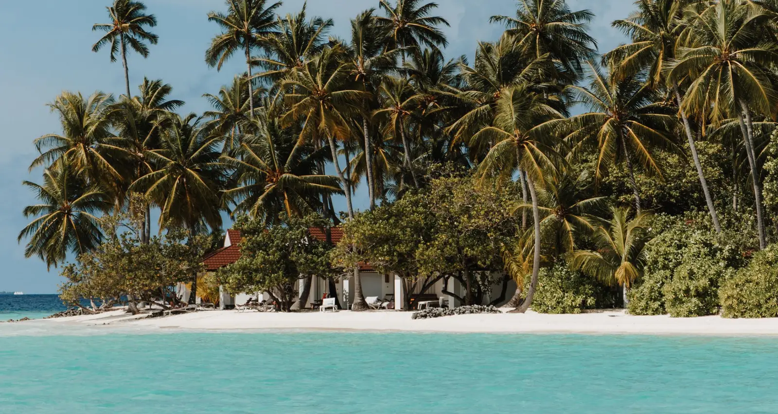 A villa on the beach among the palms, with the white sand and the shallow lagoon in front.