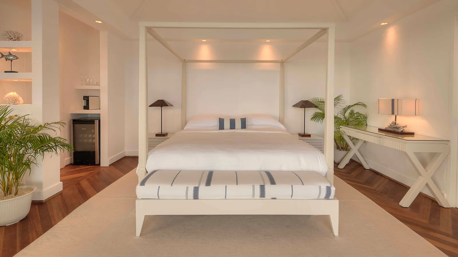 A Water Villa bedroom: the white four-poster bed, the parquet and the bedside lamps.