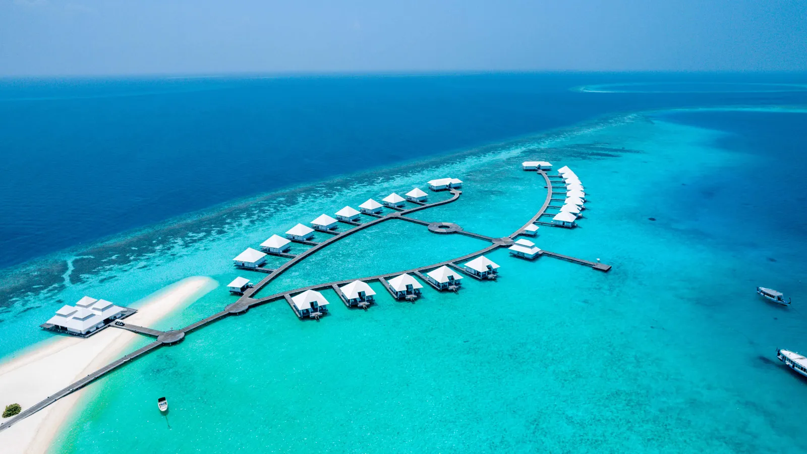 The crescent of water villas from above, the jetty running out from the beach.
