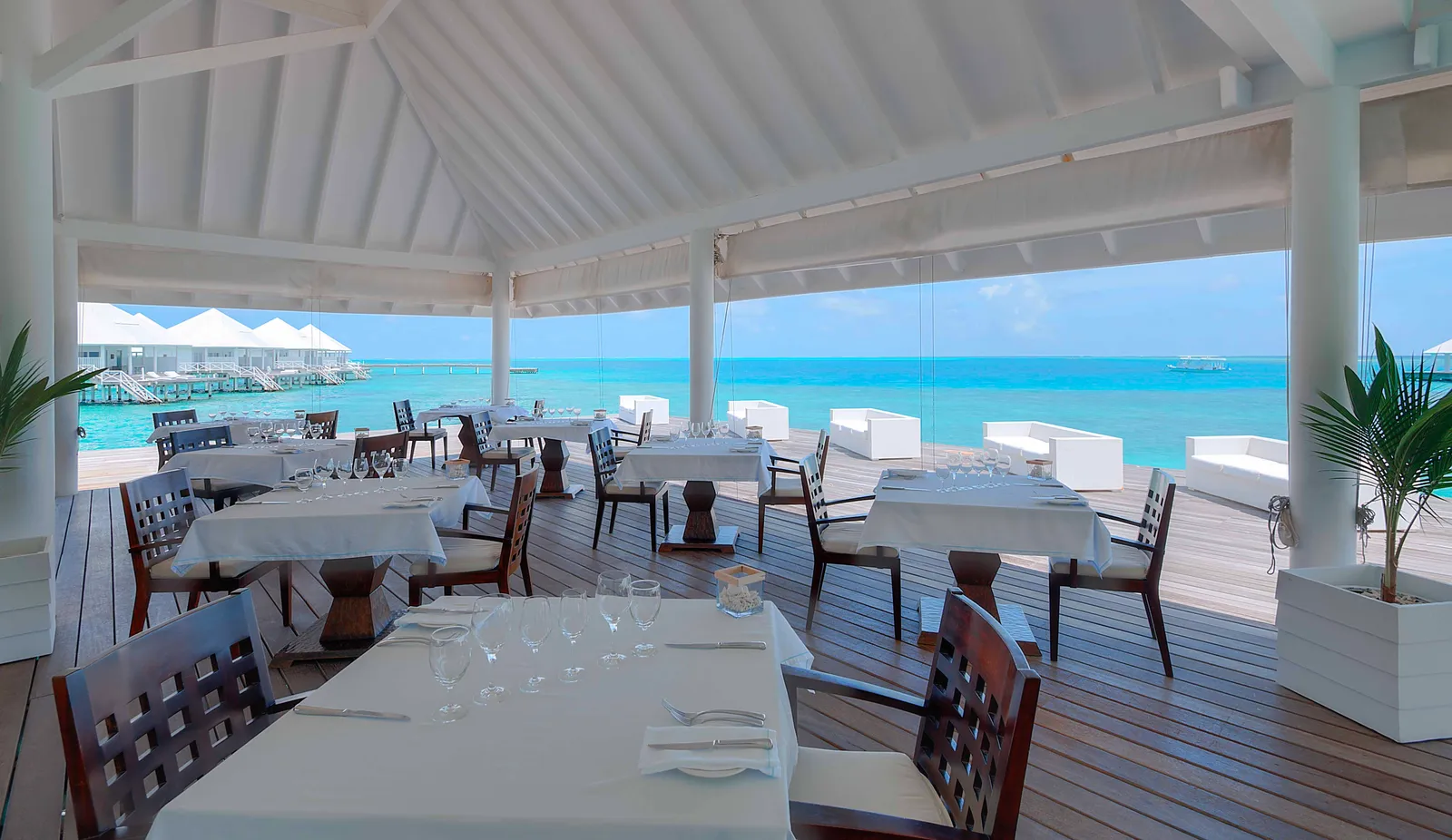 Aqua’s dining room over the lagoon, its tables laid, with the water villas behind.