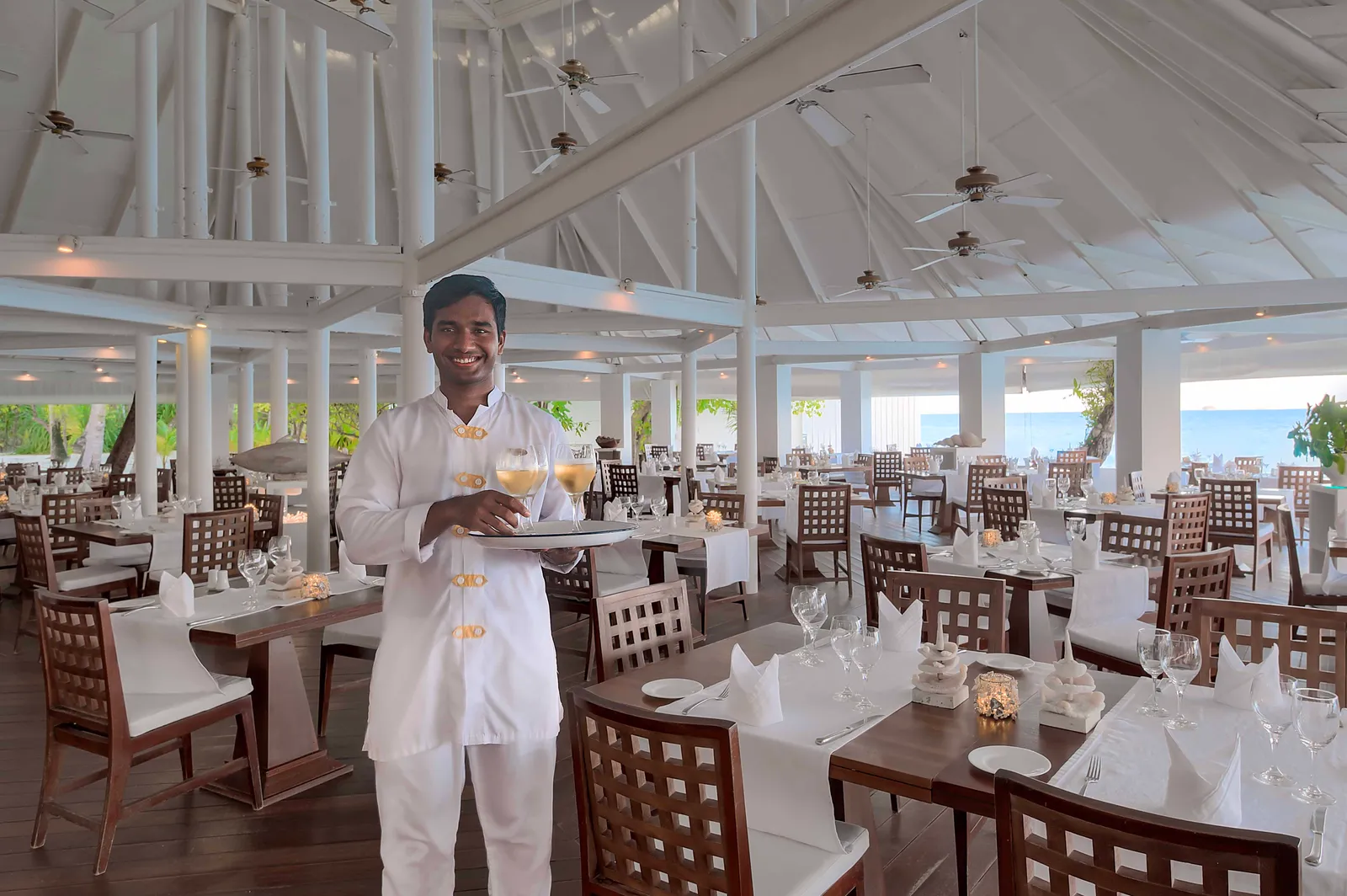 A waiter with a tray in the Maakana dining room, the main restaurant, among the laid tables.