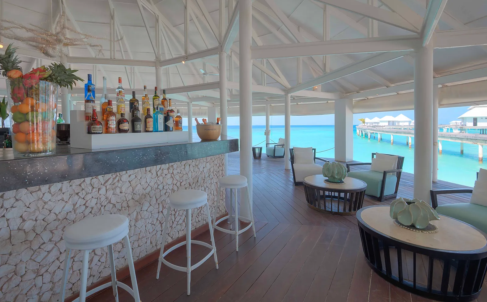 The main bar counter, with white stools and the lagoon beyond the veranda.
