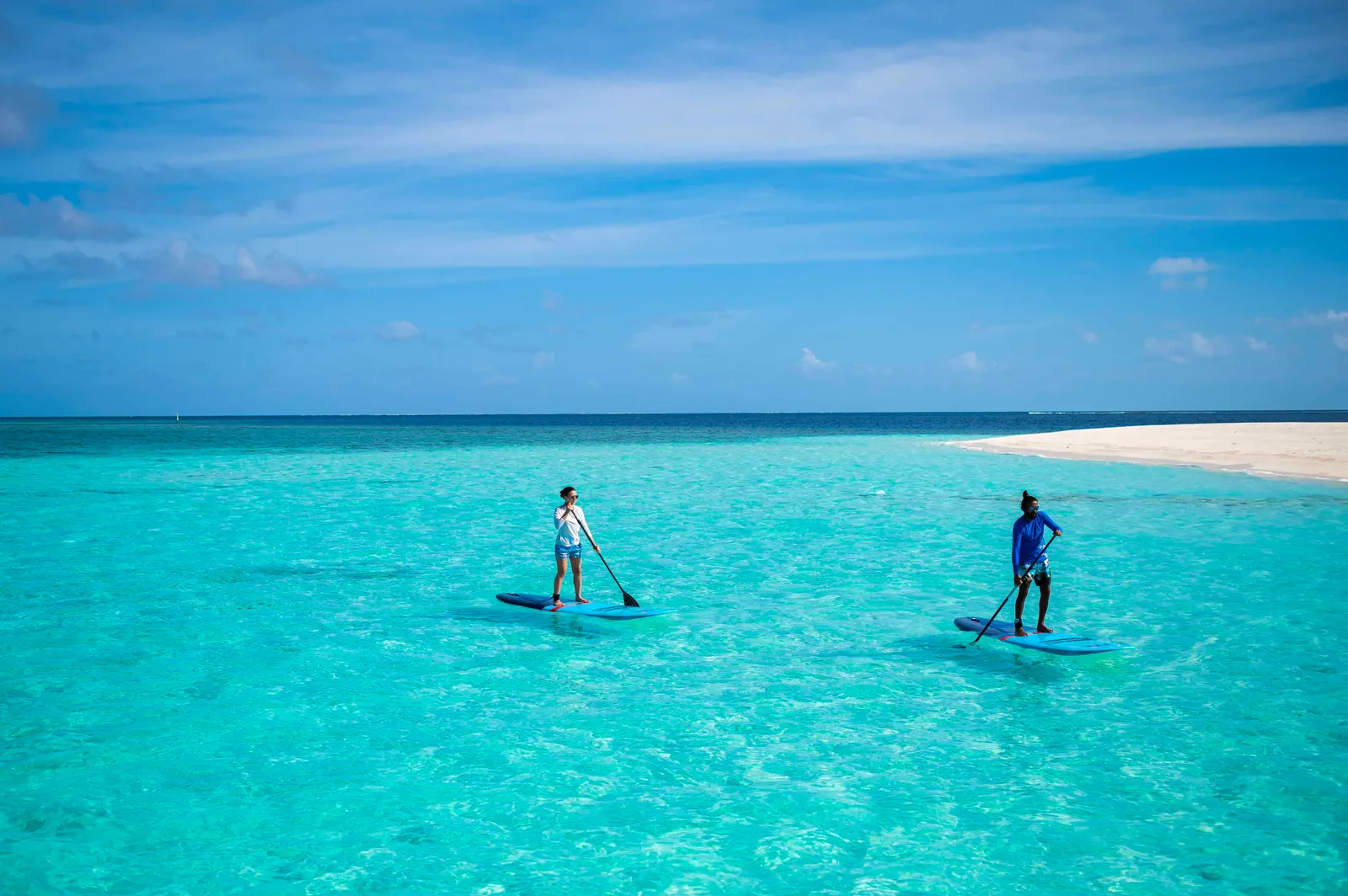 2 people on paddle boards in the turquoise lagoon, with a spit of sand behind.