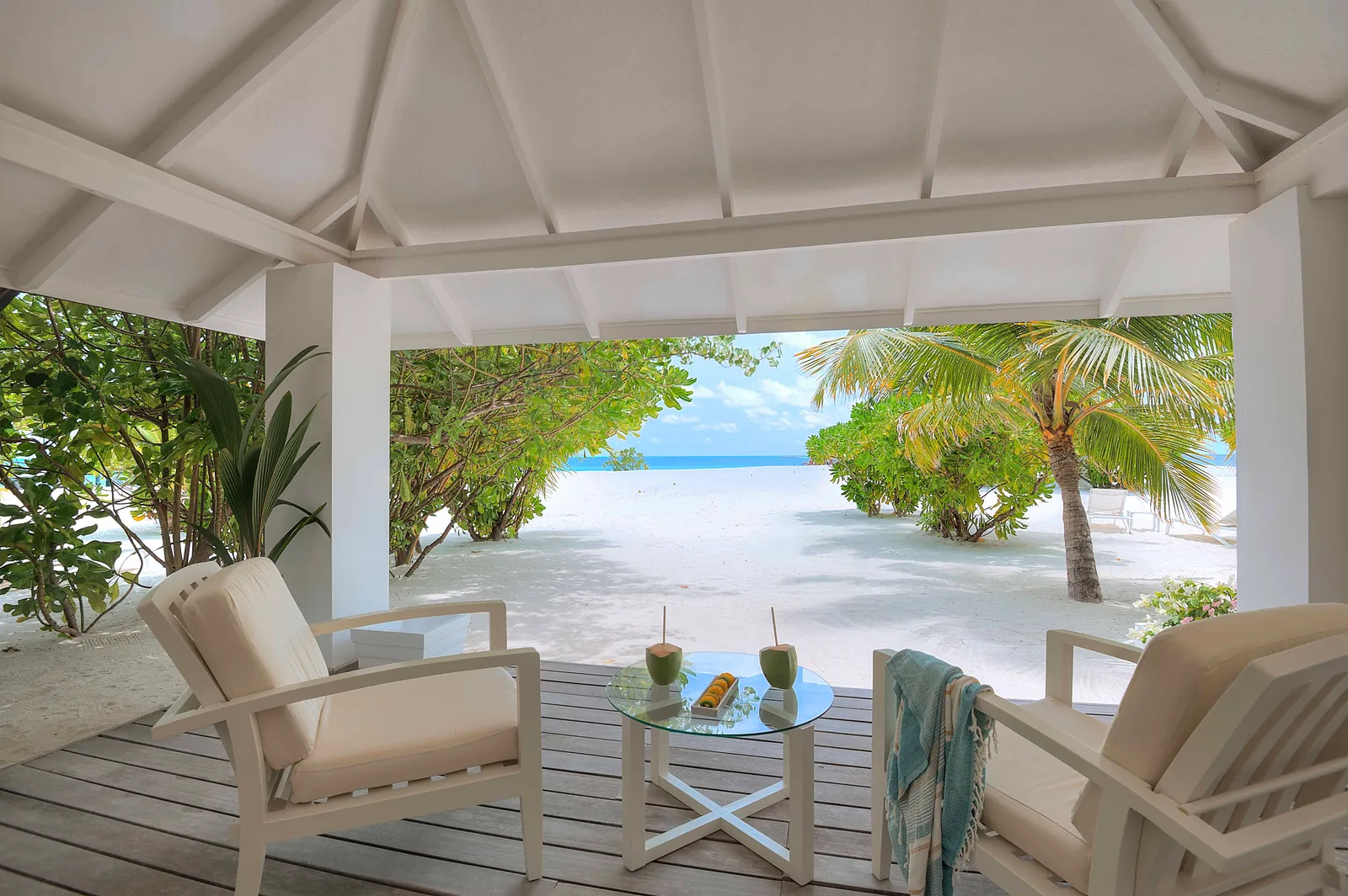 A beach suite’s covered veranda, with armchairs and the white sand ahead.