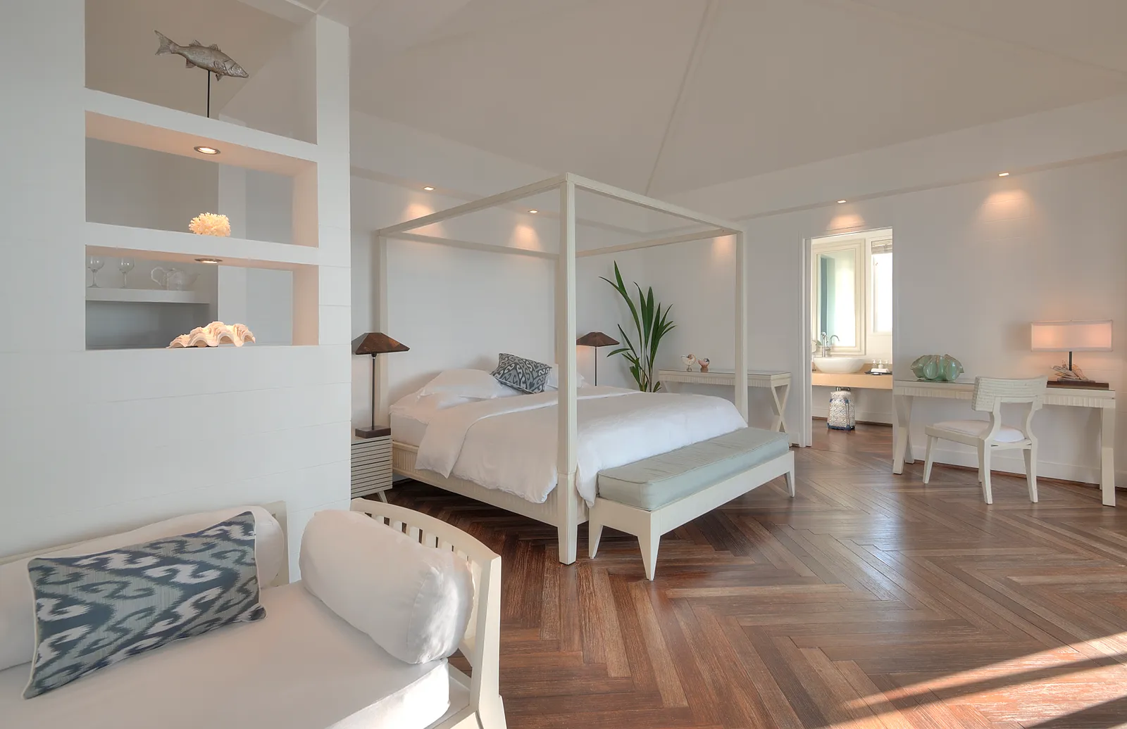 A Water Villa bedroom: the four-poster bed, the parquet and the glass doors onto the deck and the sea.