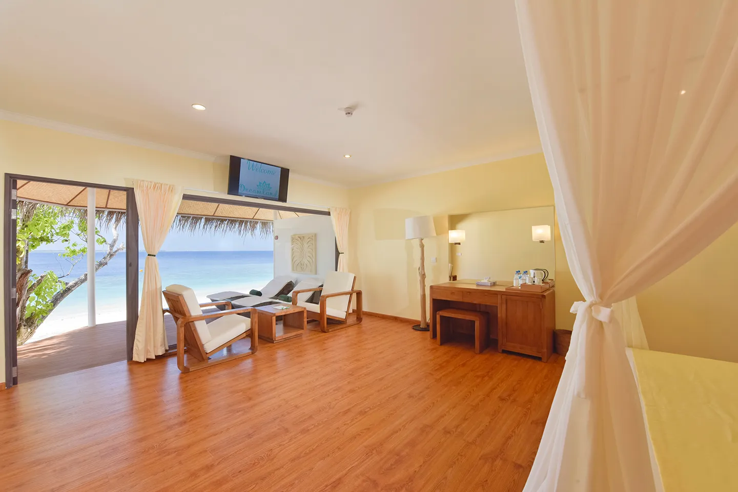 Inside a beach bungalow: the armchairs, the desk and the television, and the glass doors open onto the terrace and the sea.