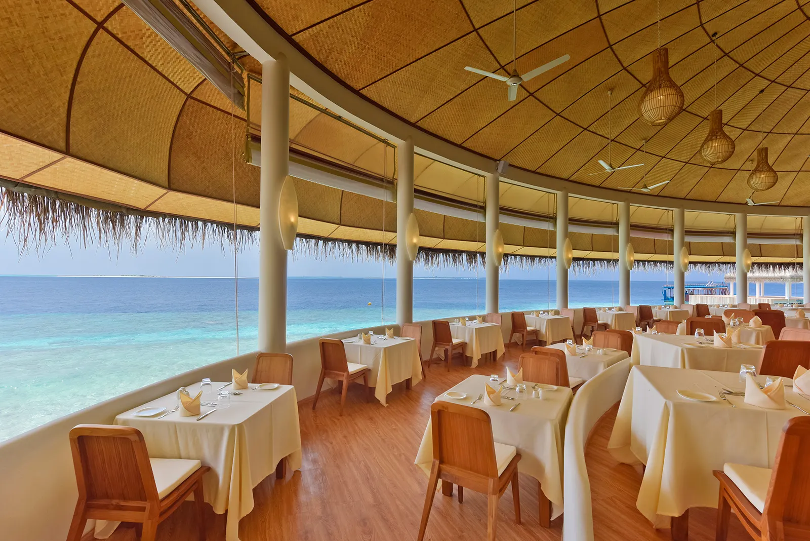 The round dining room of the Sea View Restaurant, its tables laid under the thatched roof and the windows open onto the turquoise lagoon.
