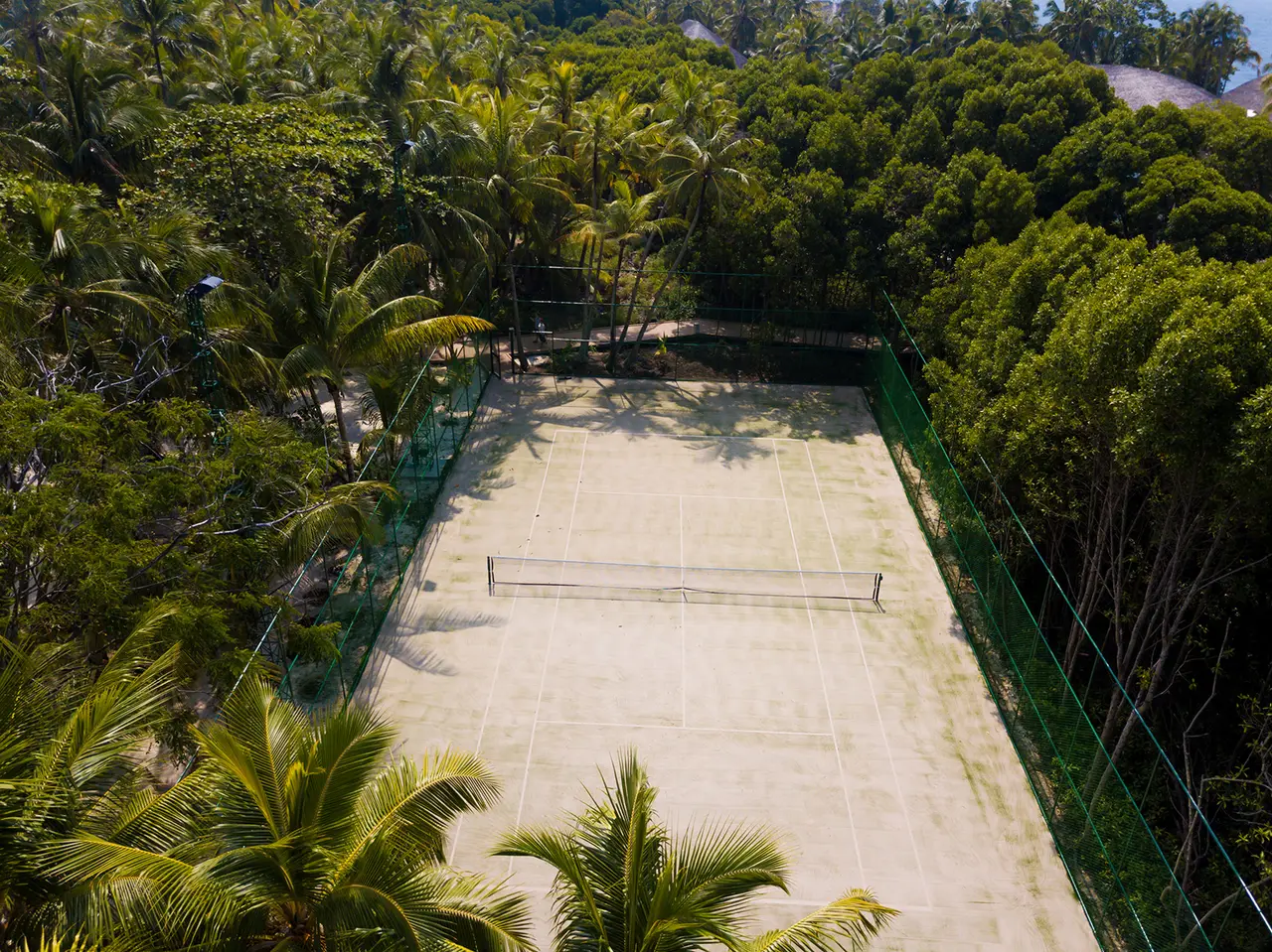 The tennis court seen from above, enclosed by palms and the island’s dense green.