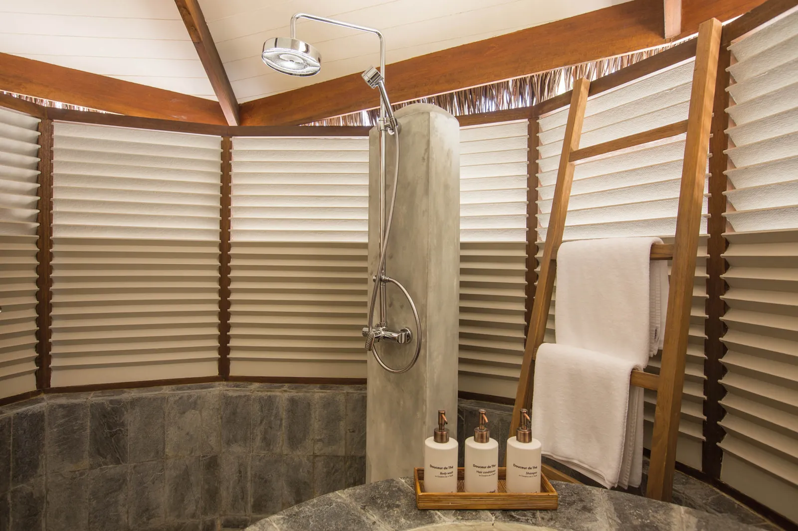 A Beach Villa’s open-air shower, between timber louvres, with white towels.