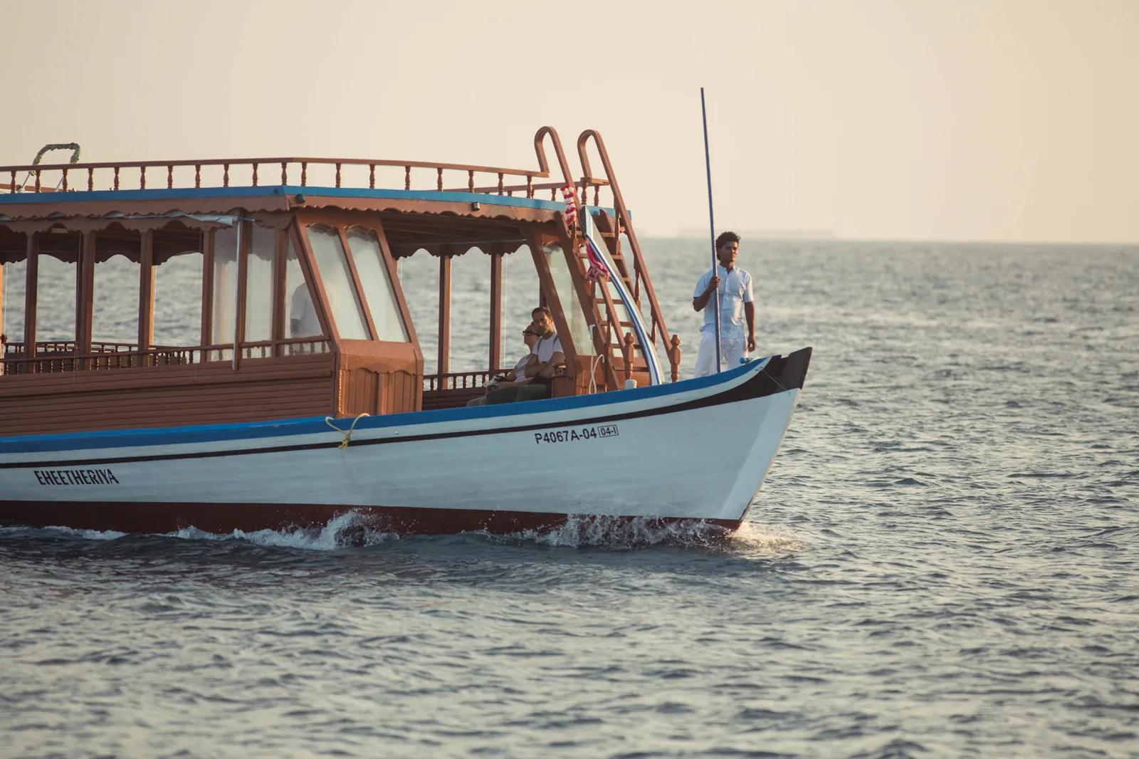 The resort’s dhoni, a 2-deck wooden boat, on calm water with the skipper at the bow.
