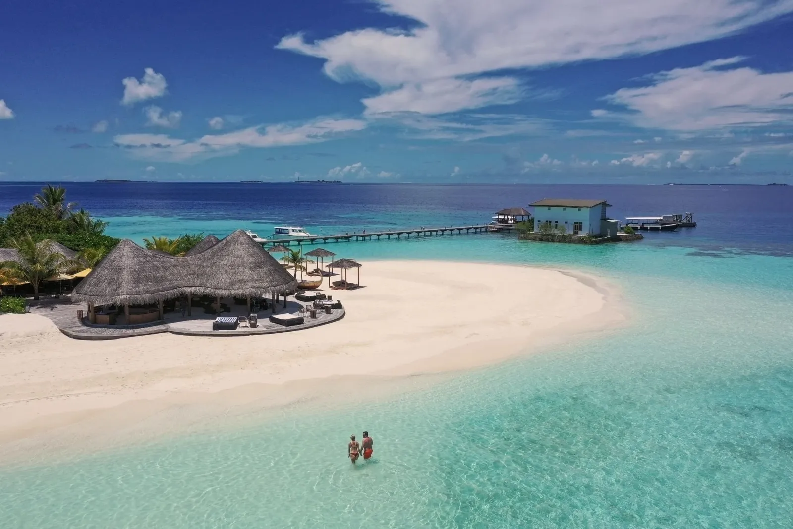The restaurant under its thatched roofs on the sandy point, the jetty running out to sea and a couple wading in the lagoon.