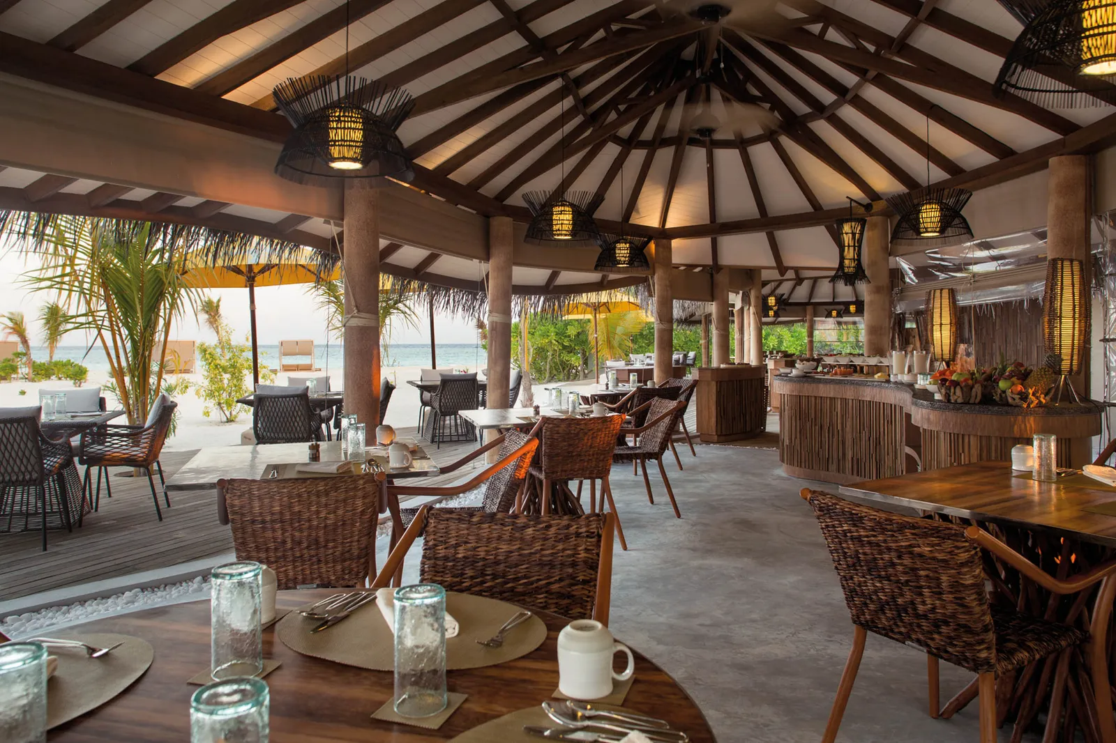 The open-air restaurant under its great timber roof, tables laid and the beach beyond the posts.