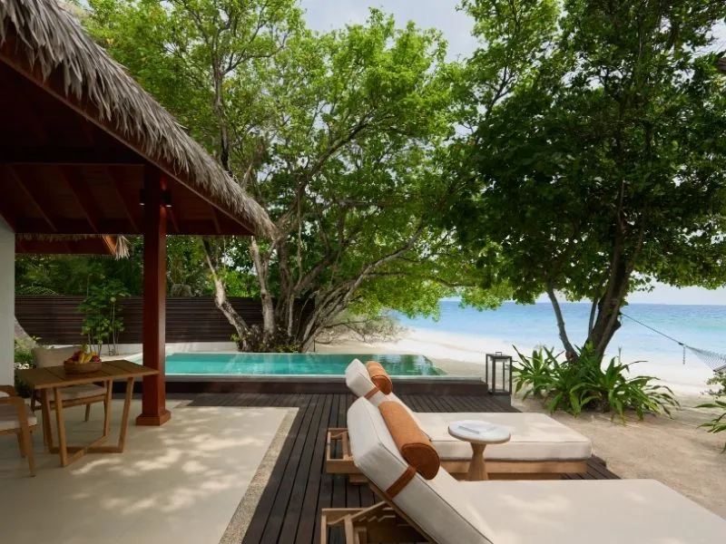 The pavilion of a Beachfront Pool Villa, with loungers, the pool and the beach beyond the hedge.