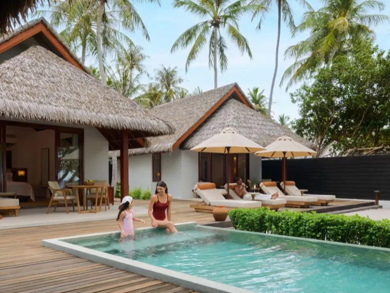The pool of a Two Bedrooms Beach Pool Villa, a mother and a girl in the water and the thatched roof behind.