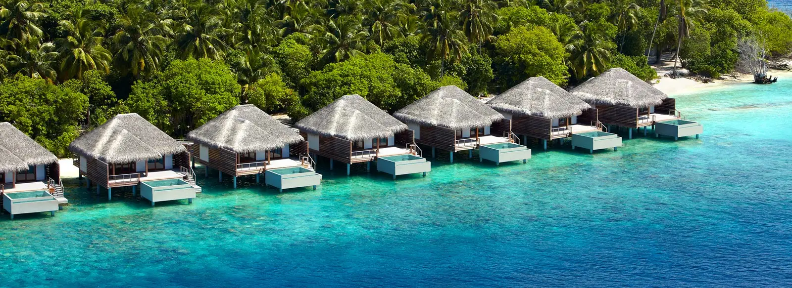 The row of water villas in front of the island’s greenery, over the turquoise lagoon.