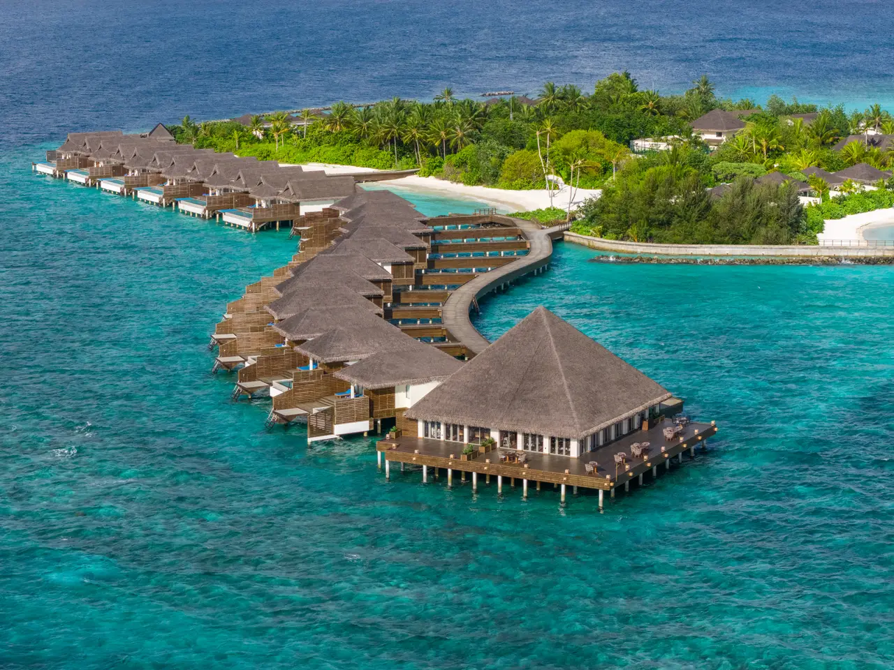 The curving walkway of water villas leading to BŌ, the restaurant over the lagoon, with the green island behind.