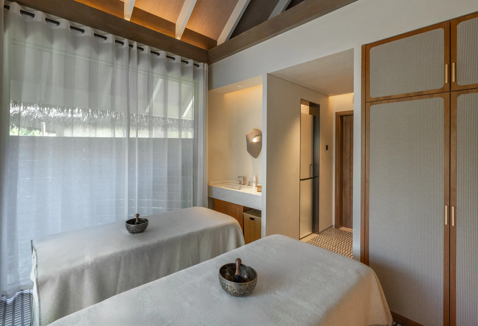 A Namm Spa couples’ room: 2 massage beds with their bowls, white curtains and timber wardrobes.