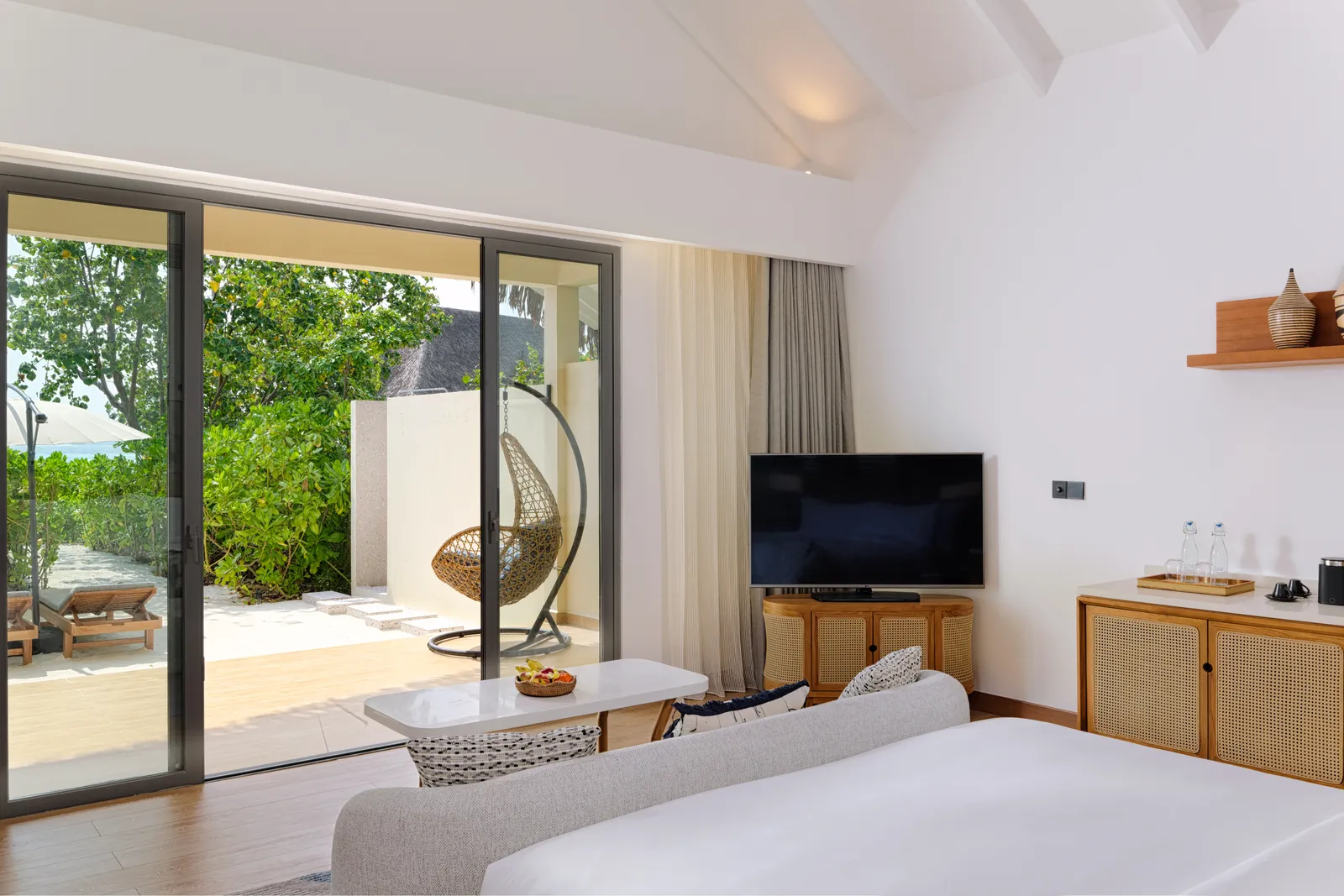 A Beach Villa: the bed, the television and glass doors open on to the terrace, a hanging chair and the garden.