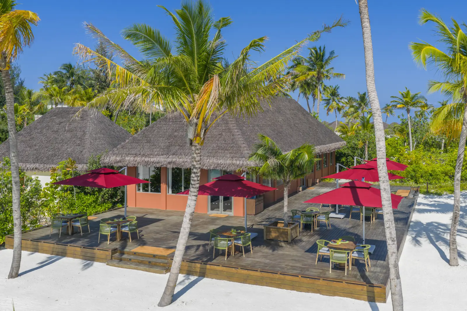SOI, the Thai restaurant on the beach: tables under red parasols in front of thatched roofs, among the palms.